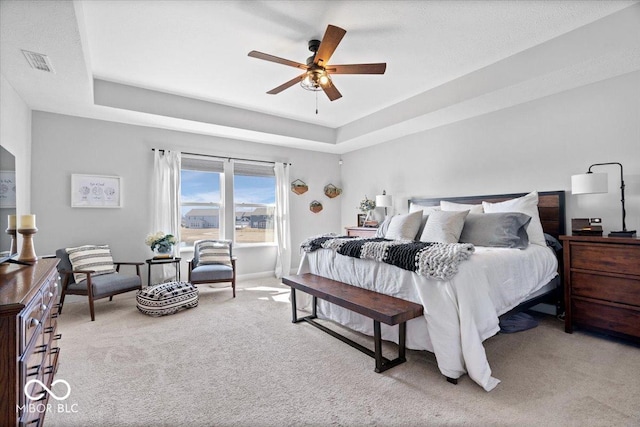 carpeted bedroom featuring a raised ceiling, baseboards, visible vents, and ceiling fan