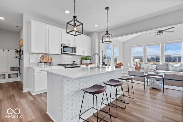 kitchen featuring stainless steel microwave, decorative backsplash, light wood-style flooring, range, and a sink