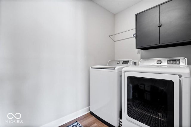 clothes washing area featuring cabinet space, washer and dryer, baseboards, and wood finished floors