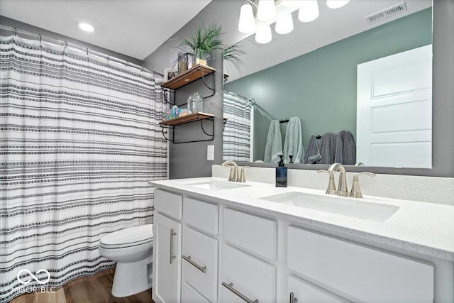 full bathroom featuring visible vents, toilet, a sink, wood finished floors, and double vanity