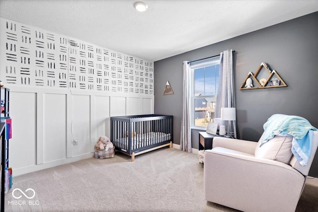 bedroom featuring a decorative wall, carpet, baseboards, and a textured ceiling