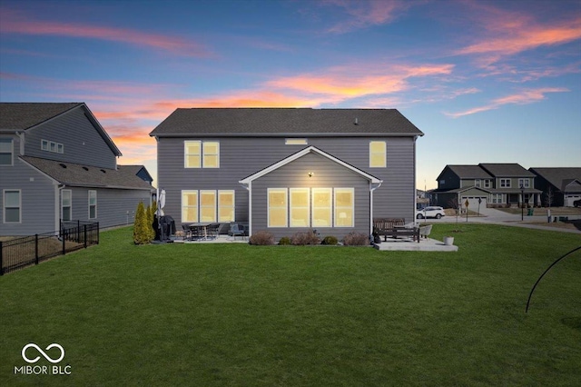 back of house at dusk featuring a yard, fence, and a patio area