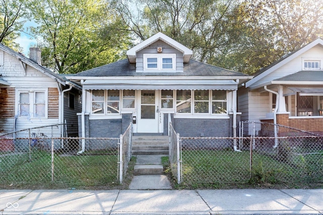 bungalow-style home with a fenced front yard, a shingled roof, and a front lawn