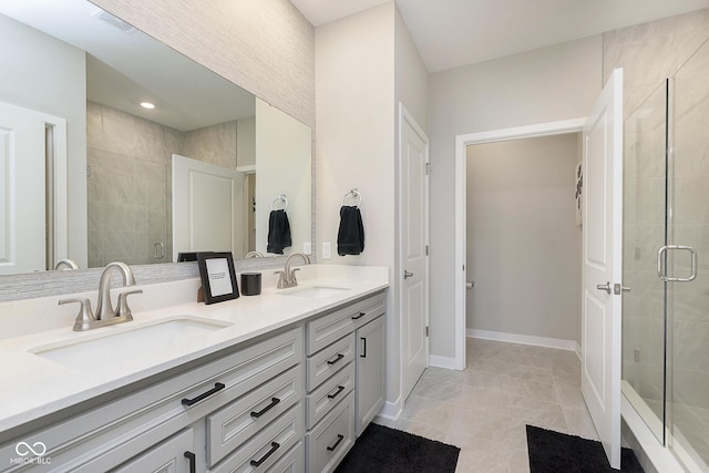 full bathroom featuring double vanity, a stall shower, baseboards, and a sink