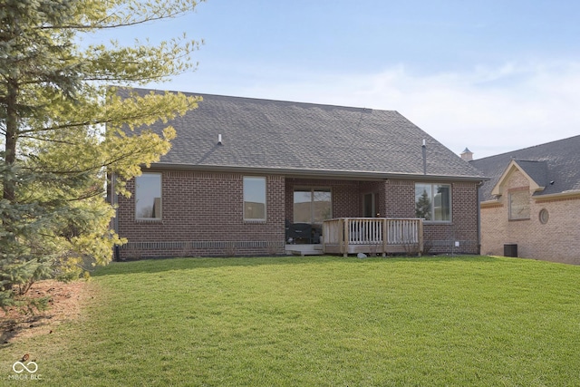 rear view of house featuring a yard, brick siding, a wooden deck, and a shingled roof