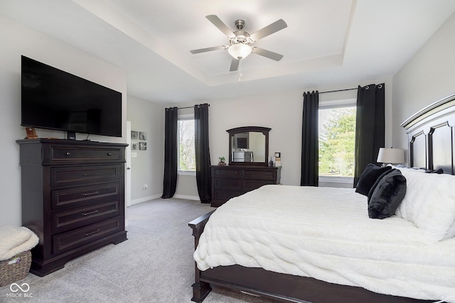 bedroom featuring multiple windows, a raised ceiling, light colored carpet, and baseboards