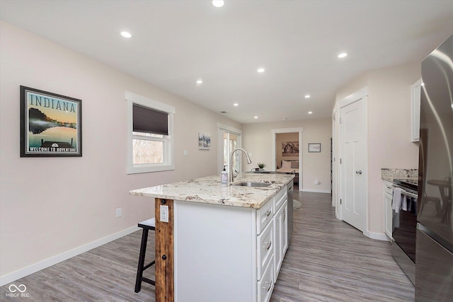 kitchen with a kitchen bar, a kitchen island with sink, a sink, white cabinetry, and stainless steel appliances