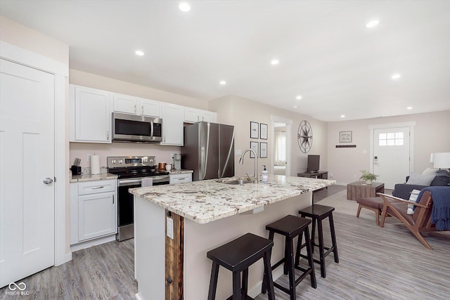 kitchen featuring a breakfast bar, a center island with sink, a sink, open floor plan, and appliances with stainless steel finishes