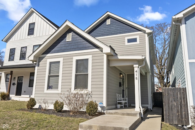 view of front of property with board and batten siding, a front lawn, fence, and covered porch