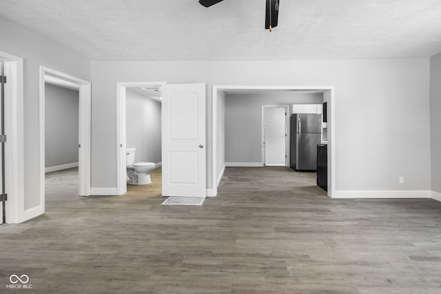 interior space with a textured ceiling, wood finished floors, baseboards, and ceiling fan