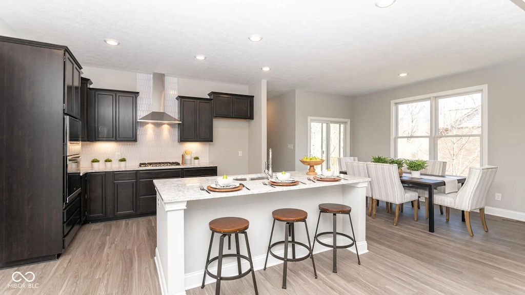 kitchen featuring light wood-type flooring, a sink, appliances with stainless steel finishes, wall chimney exhaust hood, and decorative backsplash