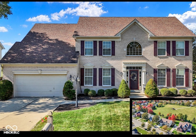 colonial house with brick siding, an attached garage, concrete driveway, and a front yard