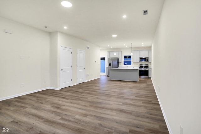 unfurnished living room with wood finished floors, visible vents, baseboards, recessed lighting, and a sink