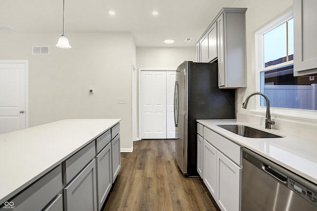 kitchen with dark wood-type flooring, gray cabinetry, a sink, appliances with stainless steel finishes, and light countertops