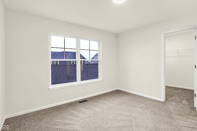 unfurnished bedroom with a walk in closet, visible vents, a closet, carpet floors, and baseboards