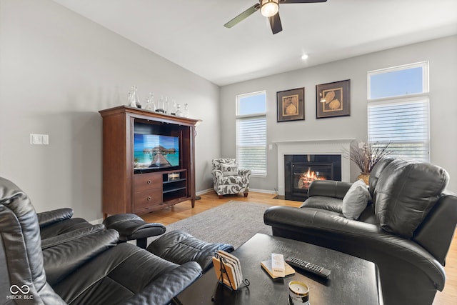 living room featuring a fireplace with flush hearth, baseboards, light wood-type flooring, and ceiling fan