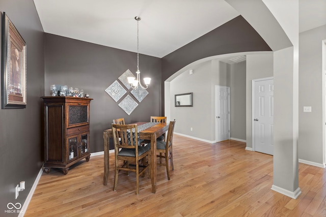 dining area featuring baseboards, arched walkways, light wood-style floors, and an inviting chandelier