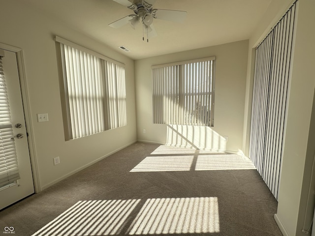 carpeted spare room with a wealth of natural light, visible vents, baseboards, and ceiling fan