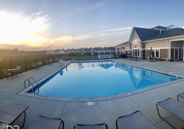 pool at dusk with a residential view, a community pool, a patio, and fence