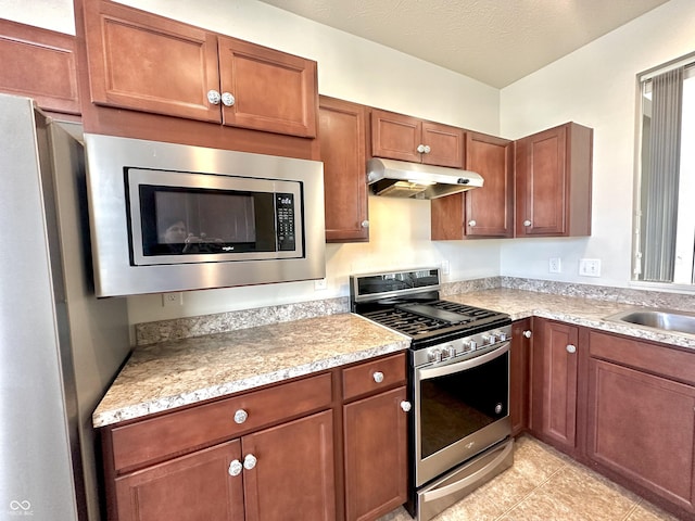 kitchen featuring under cabinet range hood, a sink, a textured ceiling, appliances with stainless steel finishes, and light tile patterned flooring