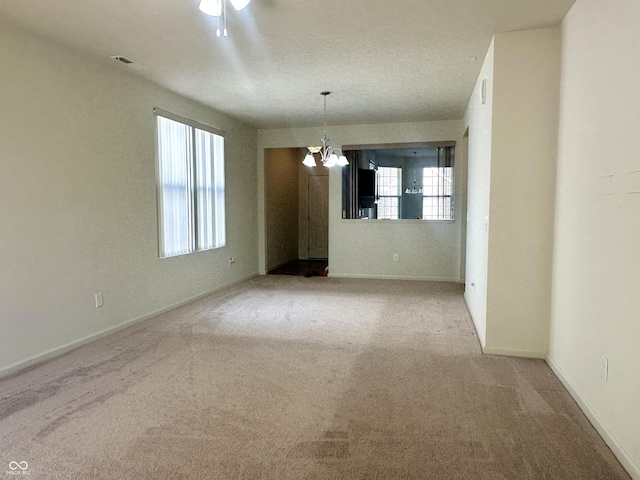 carpeted spare room featuring visible vents, baseboards, and a notable chandelier