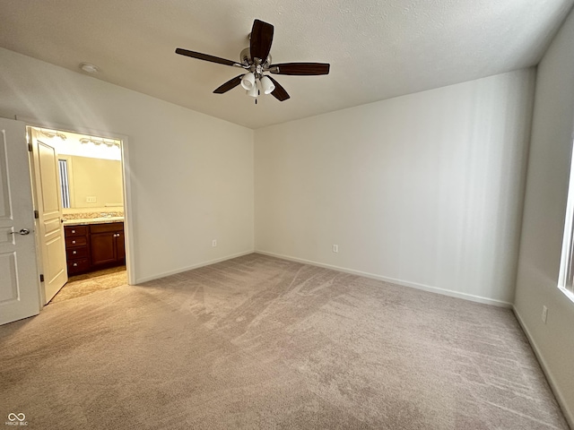 unfurnished bedroom with ensuite bath, light colored carpet, a textured ceiling, and baseboards