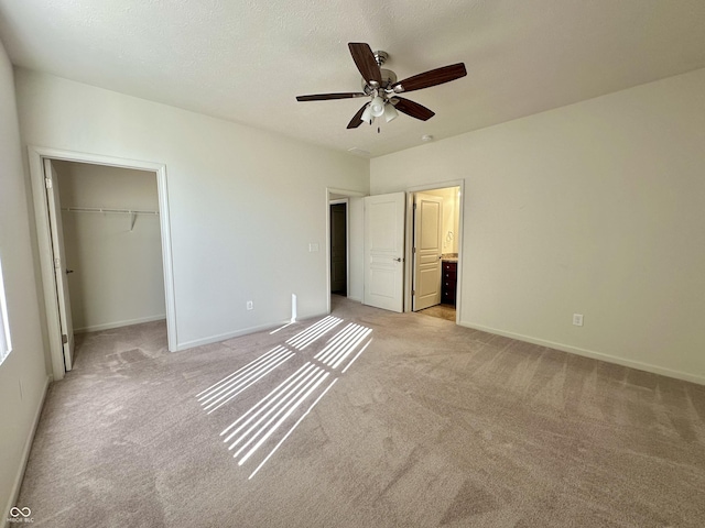 unfurnished bedroom featuring a walk in closet, light colored carpet, a closet, a textured ceiling, and a ceiling fan