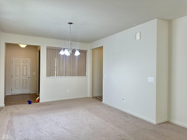 carpeted empty room featuring a notable chandelier, baseboards, and a textured ceiling