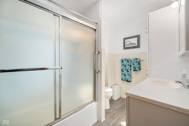 bathroom with toilet, wood finished floors, tile walls, enclosed tub / shower combo, and vanity