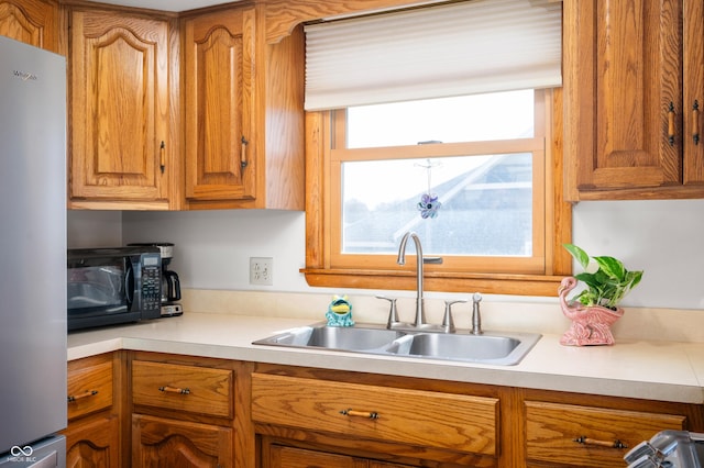 kitchen with a sink, brown cabinetry, light countertops, and freestanding refrigerator