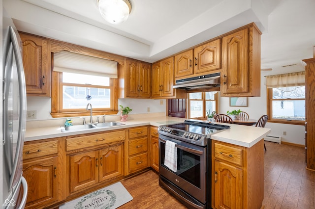 kitchen with light wood finished floors, under cabinet range hood, appliances with stainless steel finishes, a peninsula, and a sink