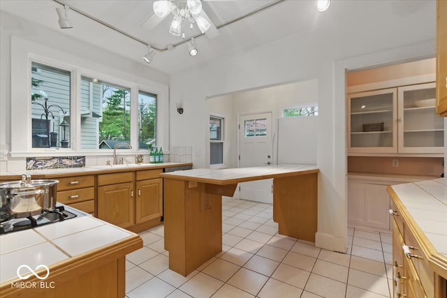 140 E 44th St, Indianapolis, IN 46205 - kitchen with light tile patterned floors, glass insert cabinets, a sink, tile counters, and a ceiling fan