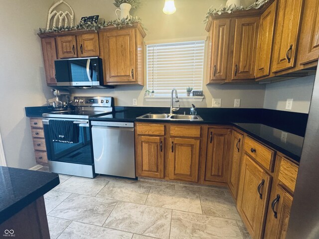 kitchen with a sink, dark countertops, appliances with stainless steel finishes, and brown cabinetry