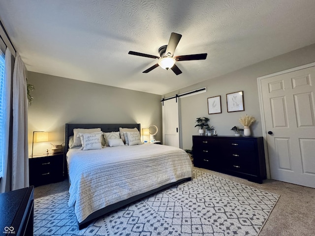 bedroom with ceiling fan, a barn door, light colored carpet, and a textured ceiling