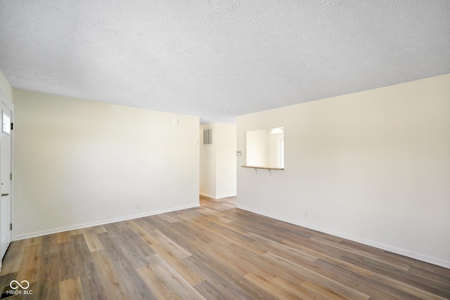 spare room with visible vents, a textured ceiling, baseboards, and wood finished floors