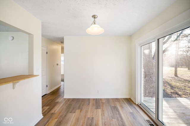 unfurnished dining area with visible vents, plenty of natural light, a textured ceiling, and light wood finished floors