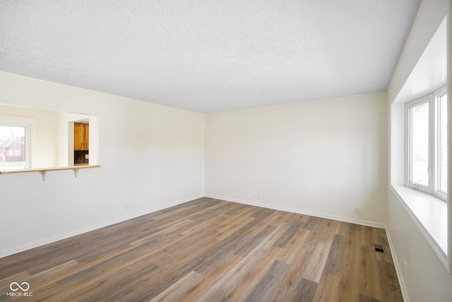 empty room with a textured ceiling, baseboards, and wood finished floors