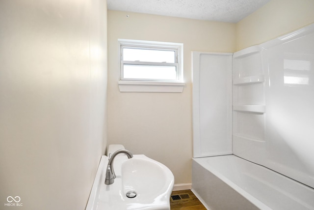 full bathroom featuring visible vents, baseboards, wood finished floors, a textured ceiling, and a sink