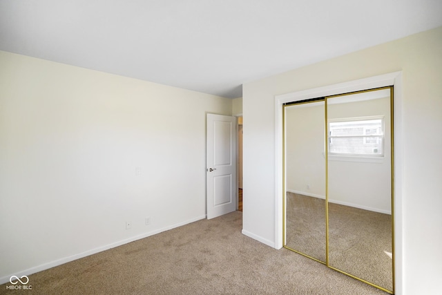 unfurnished bedroom featuring baseboards, a closet, and light carpet