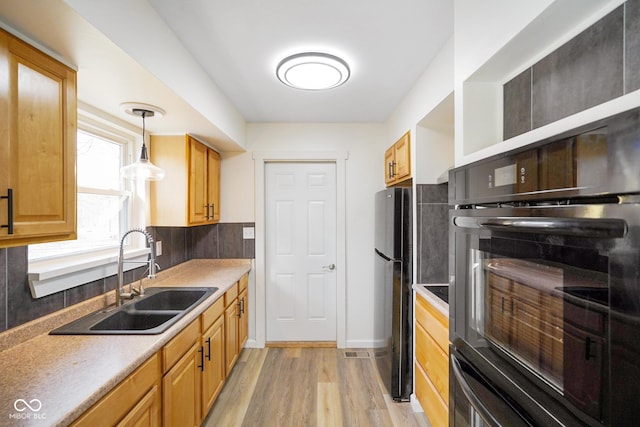 kitchen featuring decorative backsplash, light wood-style floors, hanging light fixtures, black appliances, and a sink