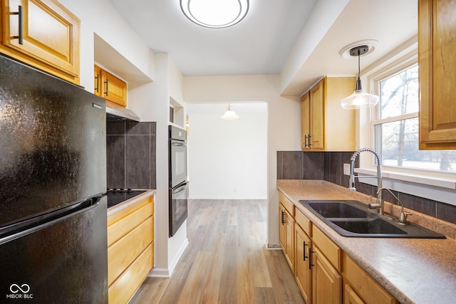 kitchen with black appliances, light wood-style flooring, a sink, under cabinet range hood, and hanging light fixtures