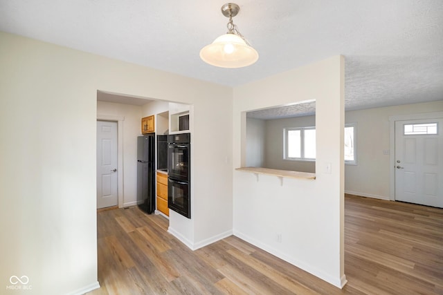 kitchen featuring light wood-type flooring, black appliances, light countertops, baseboards, and hanging light fixtures