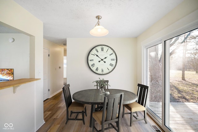 dining room with wood finished floors, visible vents, a wealth of natural light, and a textured ceiling