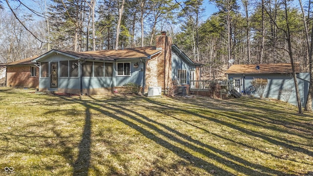 back of property with central AC unit, a sunroom, a chimney, a lawn, and brick siding