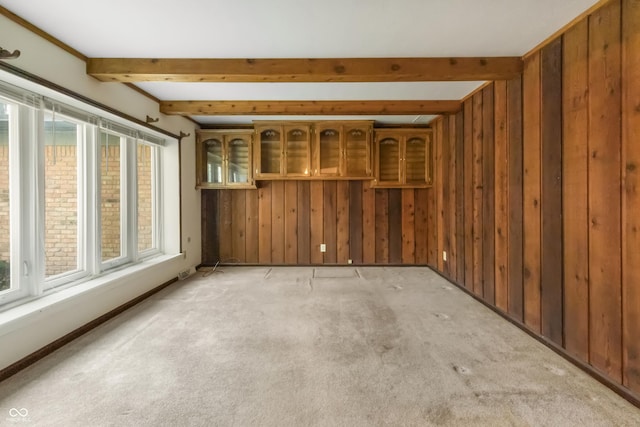 empty room with beamed ceiling, light colored carpet, and wooden walls