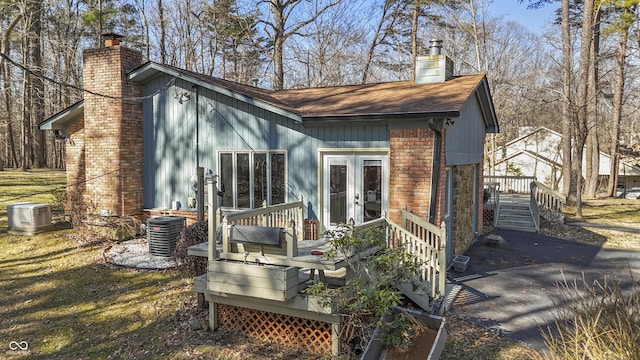 back of property with cooling unit, french doors, brick siding, and a chimney