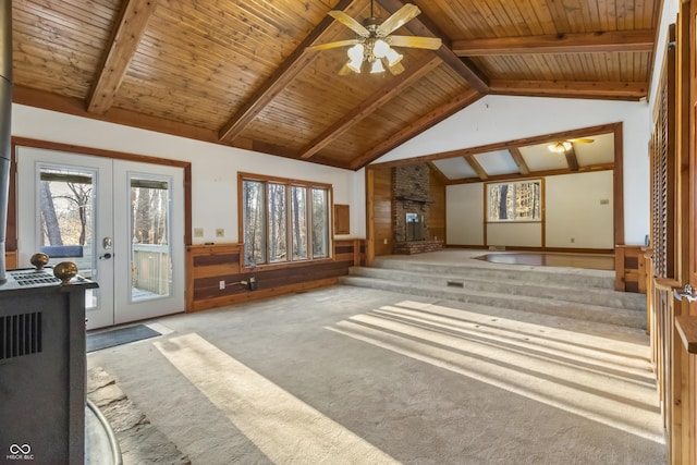 unfurnished living room with french doors, carpet floors, a fireplace, wainscoting, and vaulted ceiling with beams