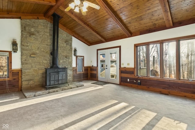 unfurnished living room with carpet, beamed ceiling, wood ceiling, wainscoting, and a wood stove