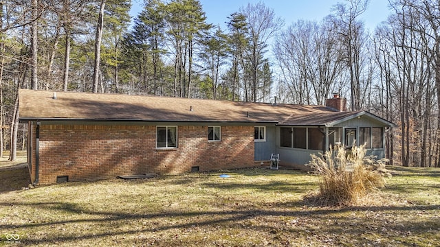 rear view of property with brick siding, a chimney, a sunroom, and crawl space