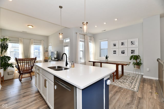 kitchen with a sink, wood finished floors, light countertops, dishwasher, and hanging light fixtures